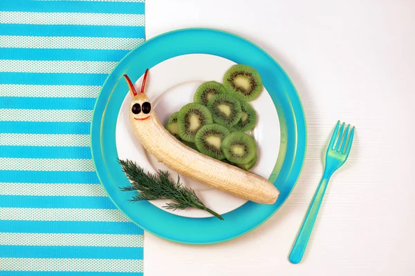 Rolig mat för barn. Söt leende snigel gjord av fruktbanan, kiwi. Hälsosam frukost för barn Stockfoto