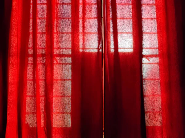 Picture of red coloured curtains in a room with sun rays visible in background shot in indoors
