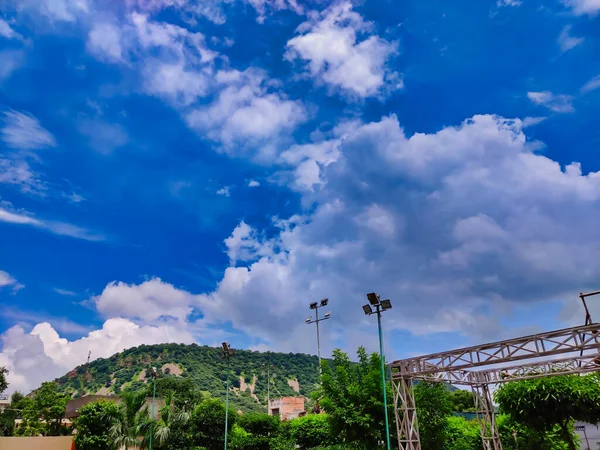 Beyaz ve gri bulutlu mavi gökyüzü. Arka planda tepeler ve ağaçlar. Aravalli Tepeleri