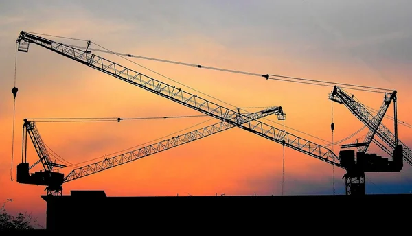 Grúas de construcción industrial y siluetas de construcción sobre el sol al amanecer. — Foto de Stock