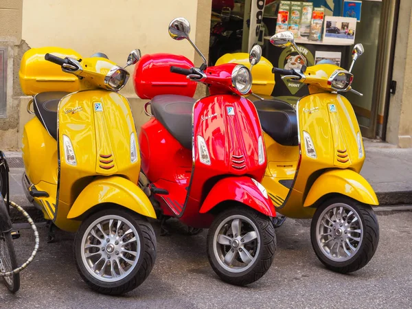 Florence, Italy - 07 21 2019: Vespa scooters standing on the street of Florence. Two yellow Vespa Sprint 150 Sport and red Vespa Primavera 150. Vespa is Italian scooter brand manufactured by Piaggio.