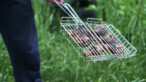 ケバブグリルネットで手と人の緑の草を背景に鶏の足を焼き — ストック動画