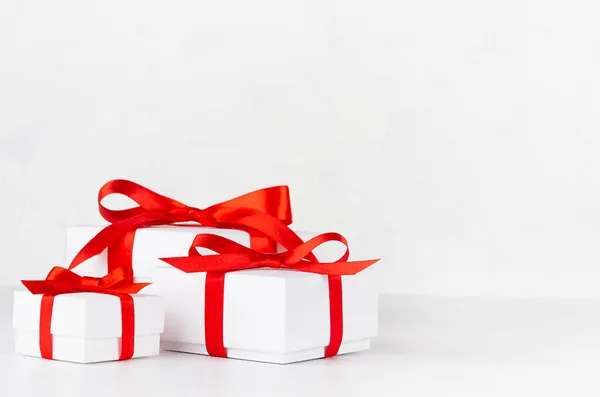 三个节日用的白色纸盒 礼物用红丝带和蝴蝶结装饰在白色桌子上 风格简约 复制空间 — 图库照片