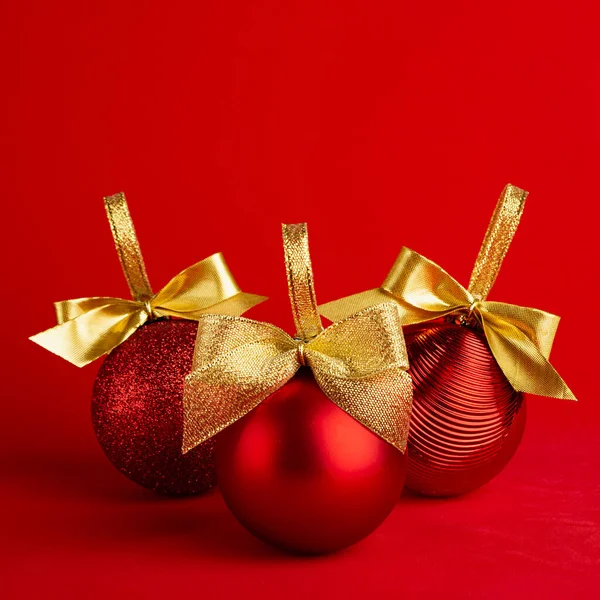 三个红色闪亮的圣诞球 金光闪闪的弓在明亮的深红色背景 正方形 简朴现代设计的新年背景招贴画 小册子 — 图库照片