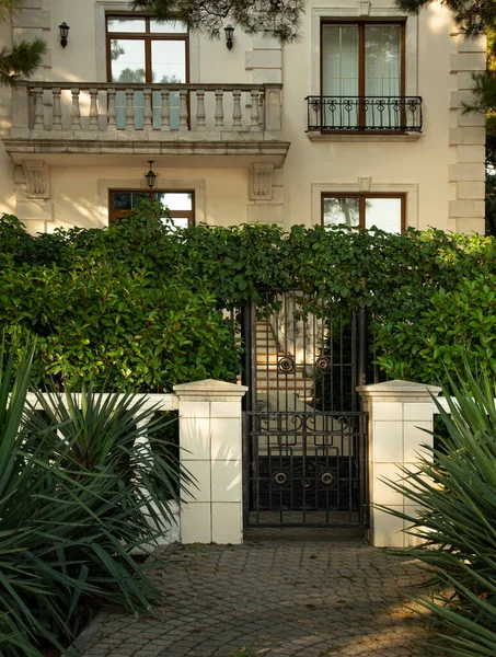 Een oud stenen huis is allemaal in groene struiken achter een oude poort, alles is ook in het groen. — Stockfoto