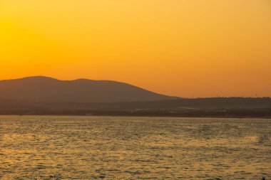 Akşam gökyüzü dağın arkasındaki batan güneşle aydınlanıyor. Denizin ve dağın üzerindeki manzara. Denizin üzerinde muhteşem bir gün batımı. Boşluğu kopyala.