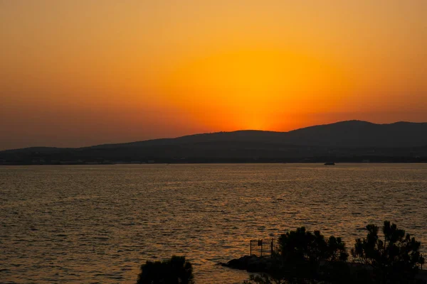 Gün batımının görkemli manzarası. Güneş, önü deniz olan bir dağın arkasında batıyor. Boşluğu kopyala.