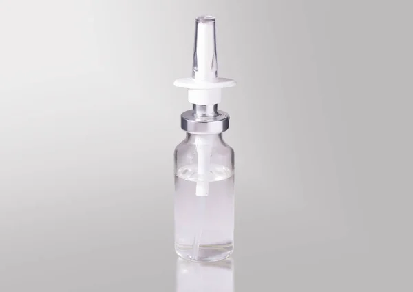 Σταγόνες μύτη σε ένα διαφανές γυάλινο μπουκάλι σε γκρι φόντο. — Φωτογραφία Αρχείου