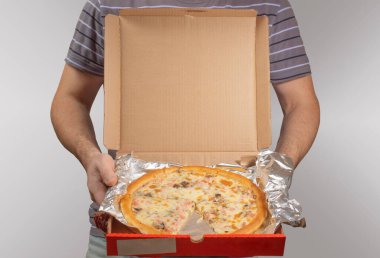 Çizgili gri tişörtlü bir adam elinde açık kırmızı bir pizza kutusu tutuyor..