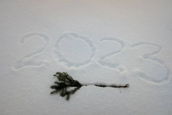 La inscripción 2023 sobre la nieve esponjosa con las ramas del árbol de Navidad, como el fondo de Año Nuevo para la tarjeta de Año Nuevo — Foto de Stock