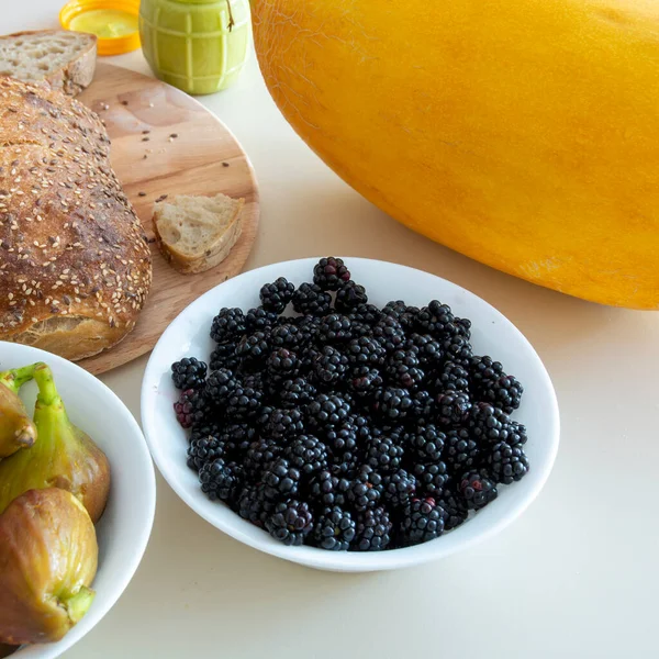 there are figs, bread and blackberries on the table, as well as a jar of honey with ginger and a large ripe melon. copy space.