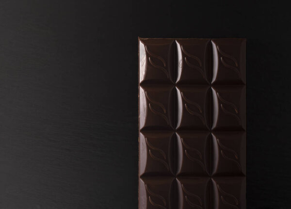 chocolate bar on a black flat stone in low light. copy space. flatlay.