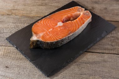 Taş bir tahtanın üzerinde biftek için taze somon dilimi. Ahşap masa geçmişi. üst- görünüm.