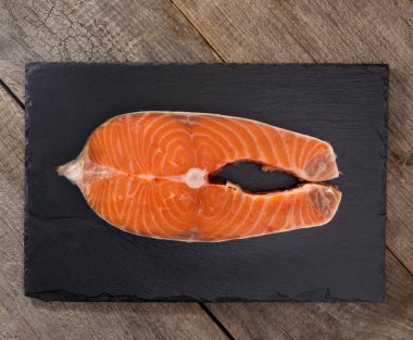 Taş bir tahtanın üzerinde biftek için taze somon dilimi. Ahşap masa geçmişi. Düz çizgi