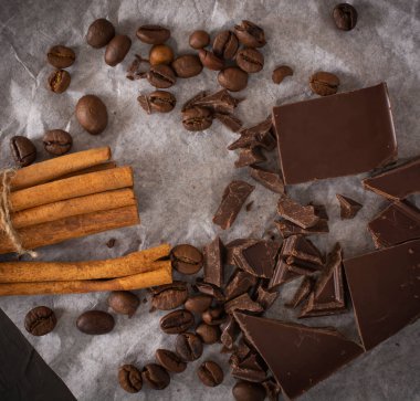 Kahve çekirdekleri ve tarçın çubuklu çikolatalar ambalaj kağıdı ve koyu arka planda. Boşluğu kopyala.