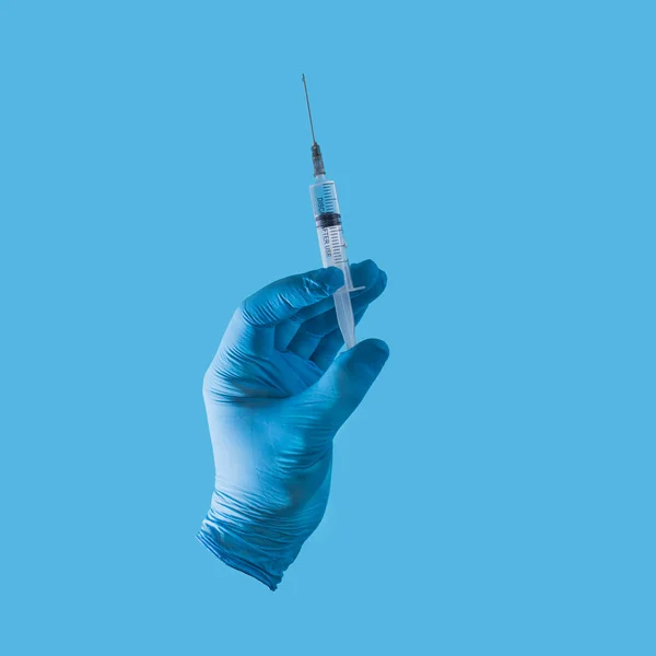 一只手在蓝色的医疗手套和蓝色背景的注射器 疫苗概念 纵向构图 — 图库照片