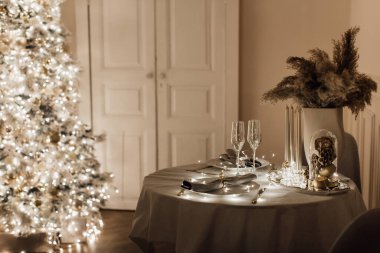 Noel 'de sıcak ve sıcak bir akşam, oturma odasının iç tasarımı, Noel ağacı süslemeli ışıklandırma tatili. Sihirli yeni yıl, yemek masası dekorasyonu şampanya parlıyor.