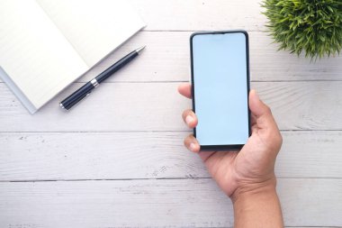 Ofis masasında boş ekranı olan akıllı telefonu tutan adamın üst görüntüsü 