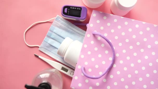 Mascarillas quirúrgicas, termómetro y desinfectante de manos sobre fondo rosa — Vídeos de Stock