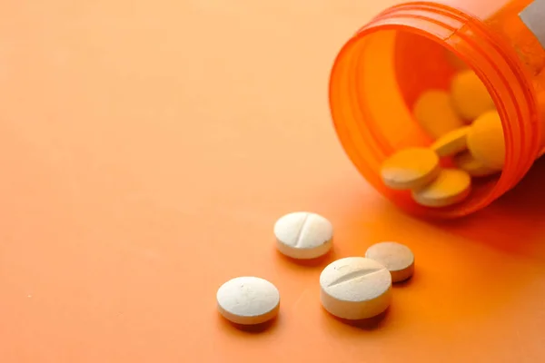 Píldoras médicas de color blanco derramamiento sobre fondo naranja — Foto de Stock