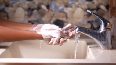 Genç adam banyoda sabunla ellerini yıkıyor. 