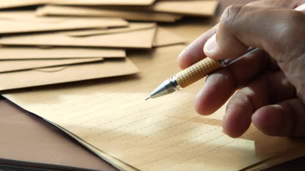 Mladý muž ruka s perem psaní na papír s obálkami na stole — Stock video