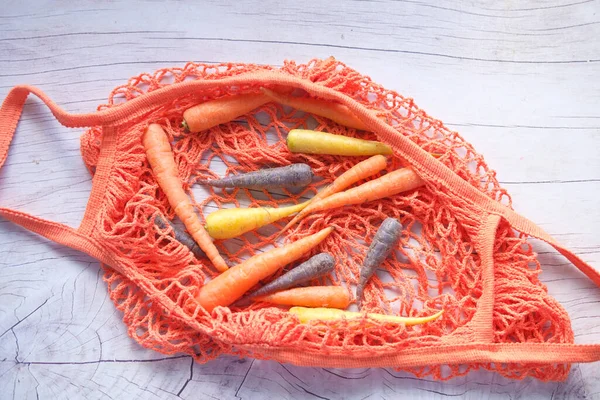 Разноцветная морковь и сумка для покупок на деревянном фоне — стоковое фото