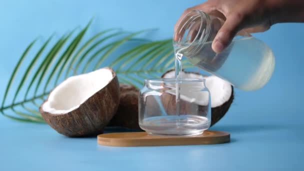 Verter aceite de coco en un recipiente sobre fondo azul — Vídeo de stock