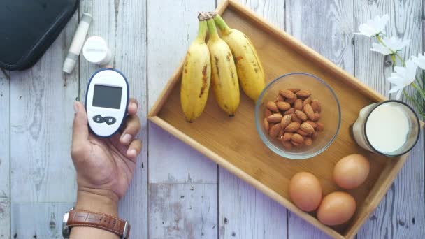 Рука чоловіка тримає лічильник глюкози з мигдальним горіхом, бананом та молоком на столі — стокове відео