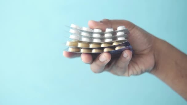Mão segurar pílulas de blister pack contra fundo azul — Vídeo de Stock