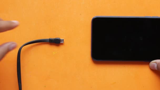 Зарядка смартфона з кабелем на кольоровому фоні — стокове відео