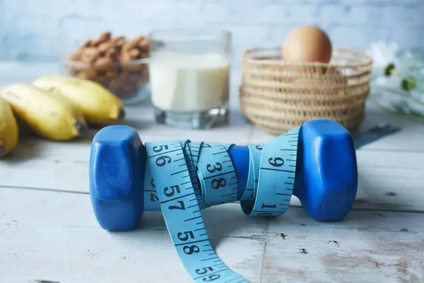 Plano de dieta com halteres, fita métrica, banana de amendoim na mesa . — Fotografia de Stock