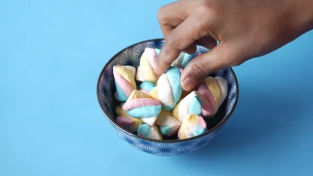 Hand pick marshmallow snoep in een kom op blauw — Stockvideo