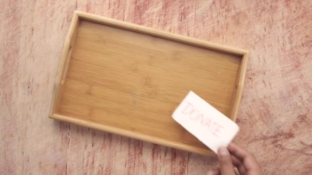 Poner un pequeño papel con la palabra donar en una bandeja en la mesa — Vídeos de Stock