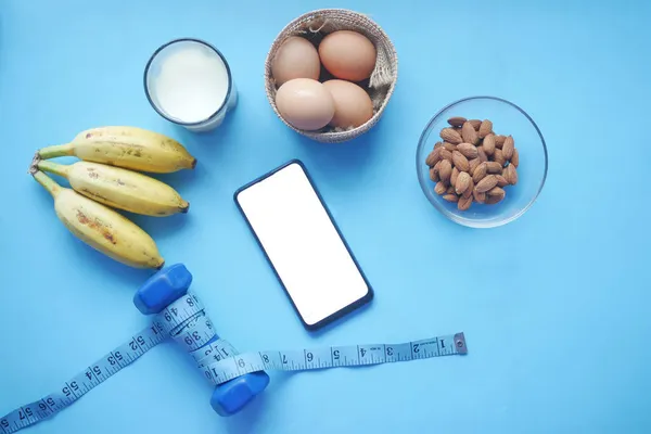 Chytrý telefon s prázdnou obrazovkou, vejci, mlékem a mandlovými oříšky v tabulce — Stock fotografie