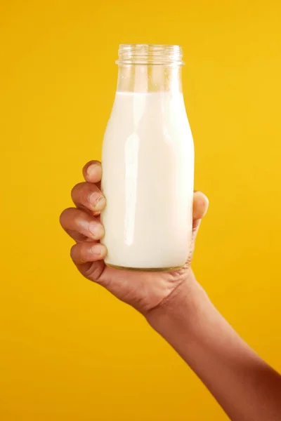 Mano tenere una bottiglia di latte su sfondo giallo — Foto Stock