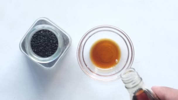 Verter los aceites de comino negro en un recipiente sobre blanco — Vídeo de stock