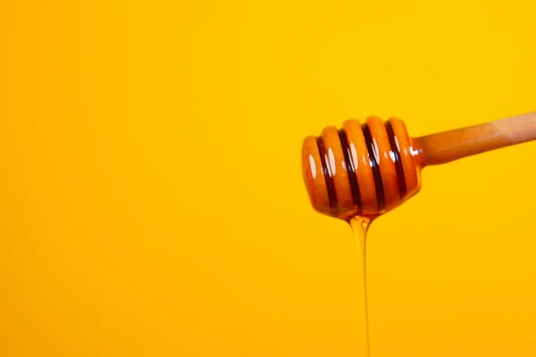 Despejar mel de colher contra fundo amarelo — Fotografia de Stock