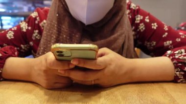 Kafede akıllı telefon kullanan yüz maskeli genç kadınlar. 