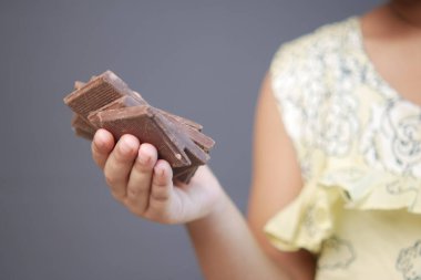 Çocuk kız, gri arka planda siyah çikolata seçiyor. 