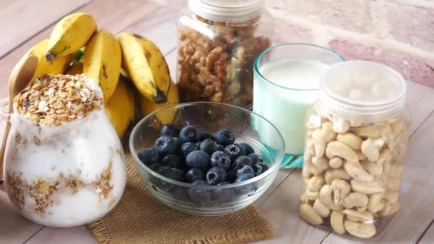 Friss kék bogyó tálban banánnal, tejjel és mandulával az asztalon — Stock videók