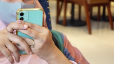 Yüzü maskeli genç kadınlar otururken akıllı telefon tutarlar. 