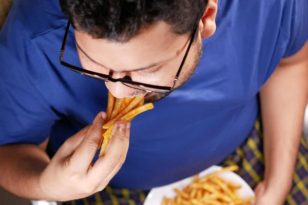 Un hombre gordo comiendo papas fritas mientras se encuentra —  Fotos de Stock
