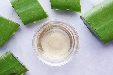 Yakın plan taze Aloe vera dilimlenmiş ve doğrama tahtasındaki bir kapta yağ var.
