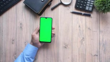 Ofis masasında akıllı telefon kullanan bir adamın üst görüntüsü. 