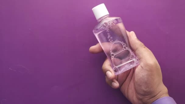Tangan memegang wadah cair obat kumur terhadap latar belakang ungu — Stok Video