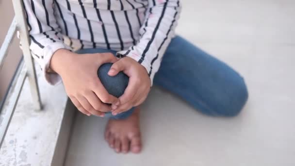 Девочка страдает от боли в коленном суставе, сидя на полу — стоковое видео