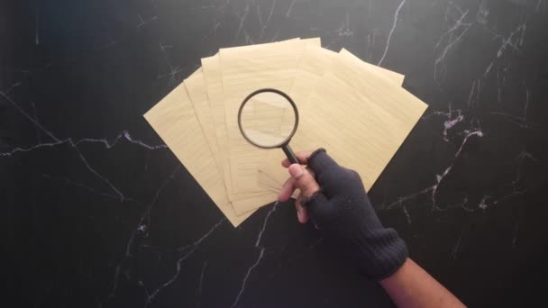 Χέρι κρατώντας μεγεθυντικό φακό κοιτάζοντας κάτι σε χαρτί — Αρχείο Βίντεο