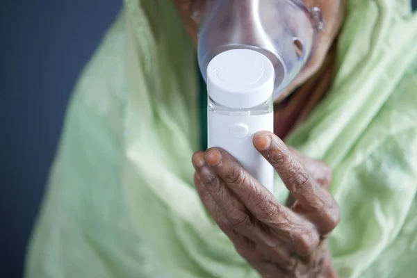 Tangan wanita senior memegang nebulizer terhadap latar belakang abu-abu muda — Stok Foto