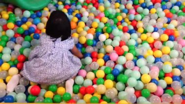 Bir sürü renkli plastik topla oynayan kız çocuğunun en üst görünümü 